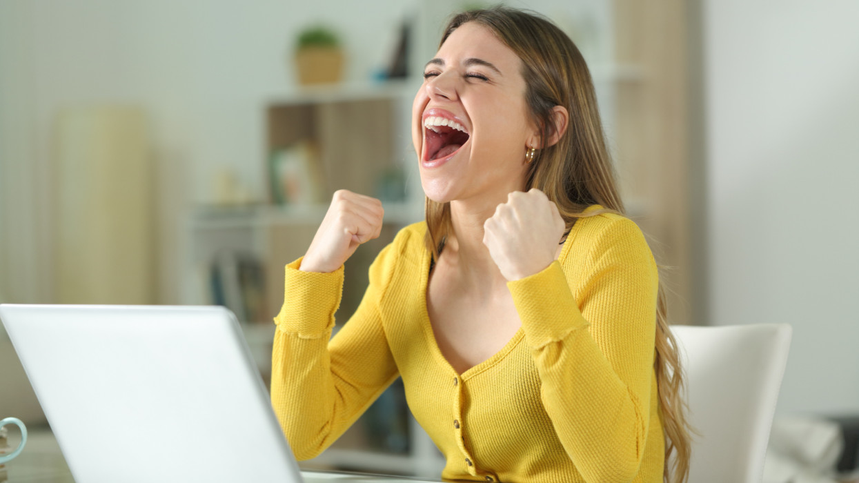 Excited woman with a laptop celebrating at home