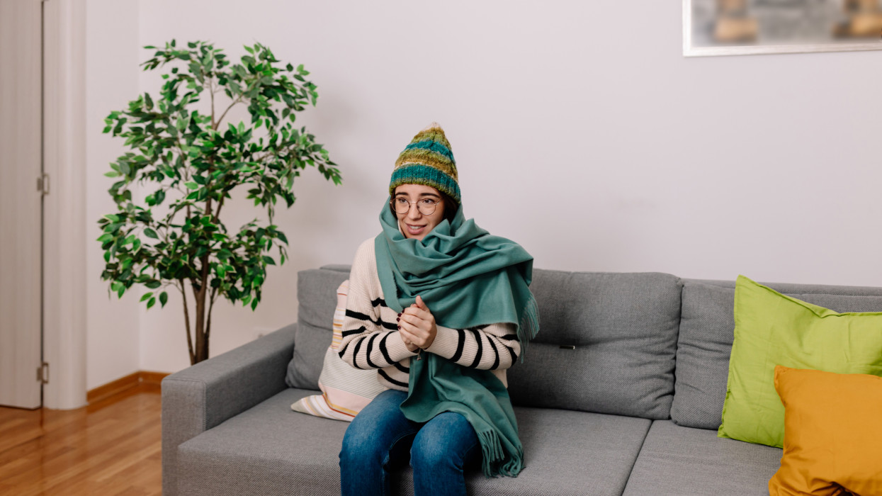 A young Caucasian woman feeling very cold at home while sitting in warm clothes