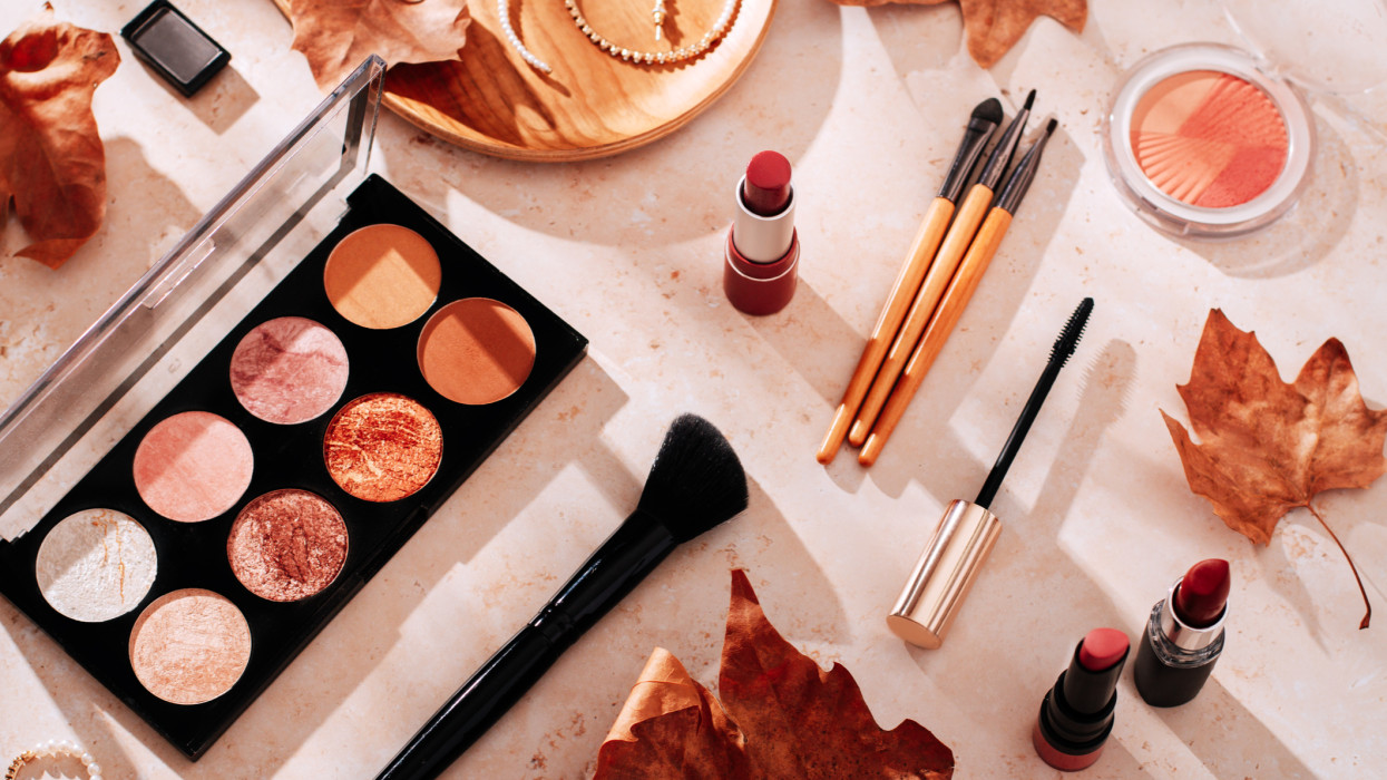 Beauty products and makeup, autumn leaves on beige background. Autumn skincare and autumn makeup concept.