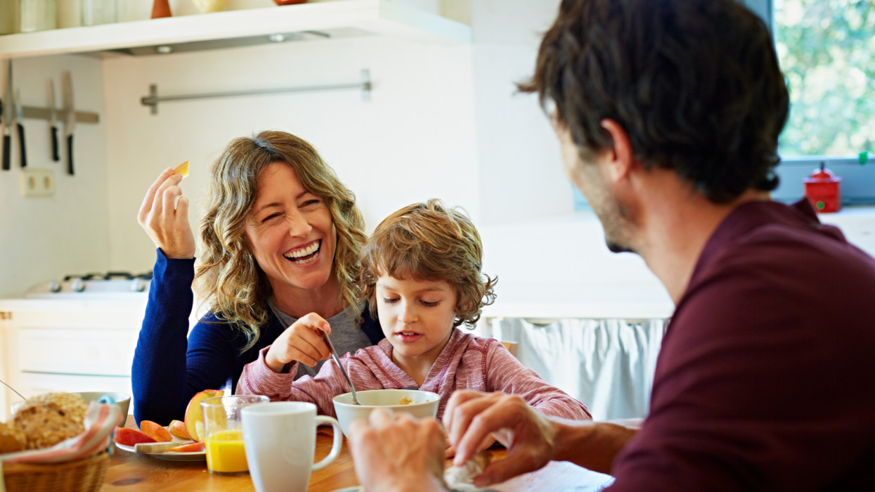 Happy family of three enjoying breakfast at table in domestic kitchen