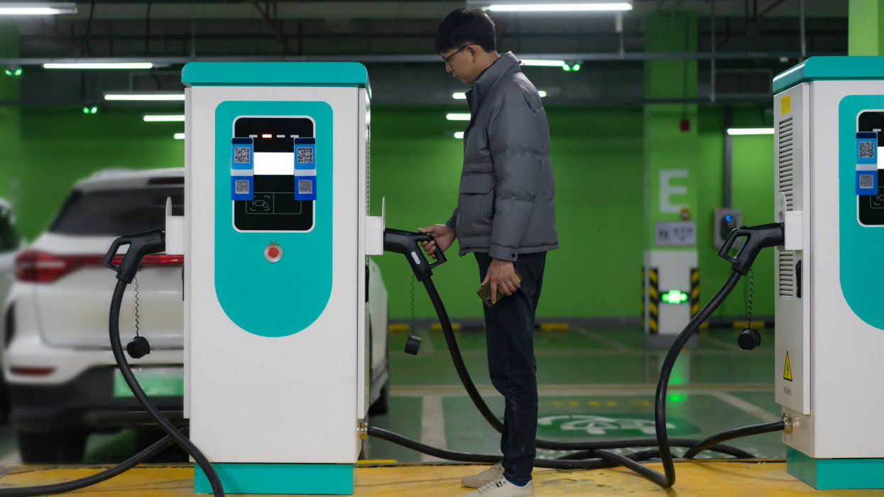 Electric car charging station, Asian man is preparing to charge his electric car, sustainable living concept