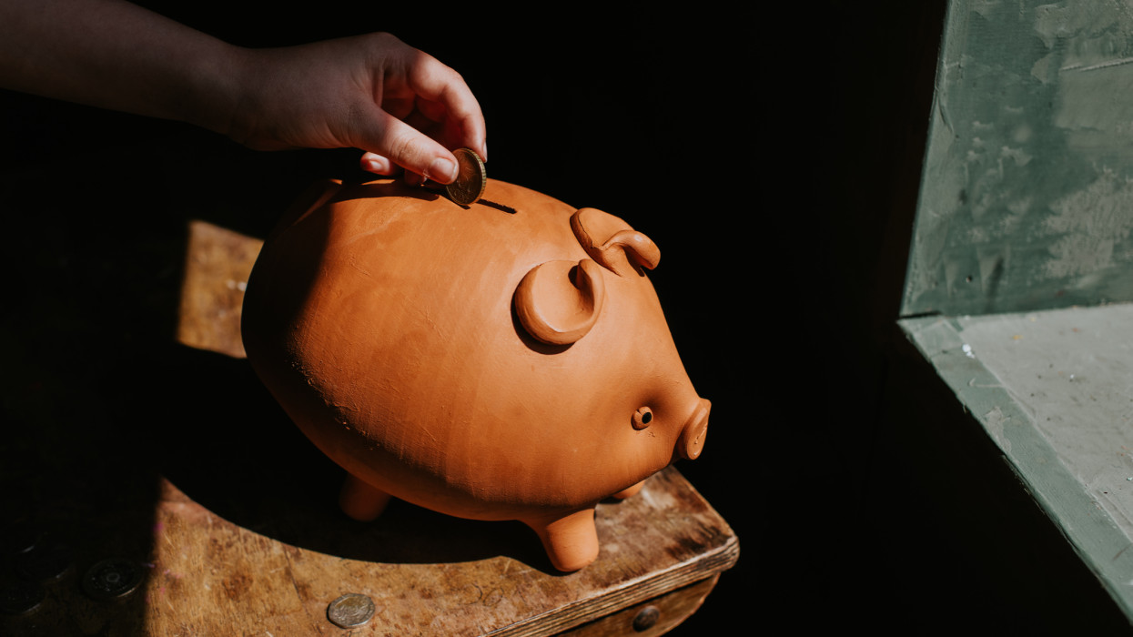 Conceptual image of a child dropping a coin into a clat piggy bank.