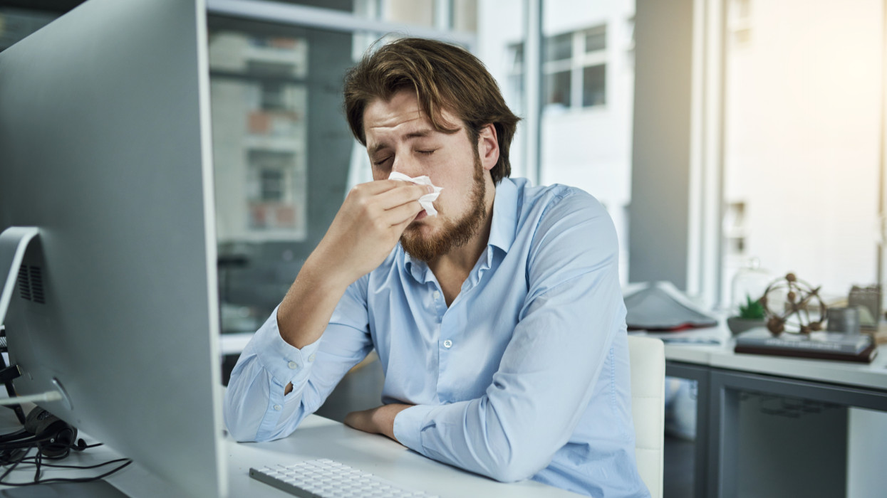 Shot of a young businessman blowing his nose in an office sick work tissue