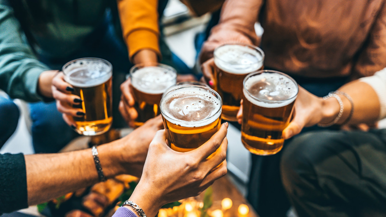 Group of friends drinking and toasting glass of beer at brewery pub restaurant- Happy multiracial people enjoying happy hour with pint sitting at bar table- Youth Food and beverage lifestyle concept