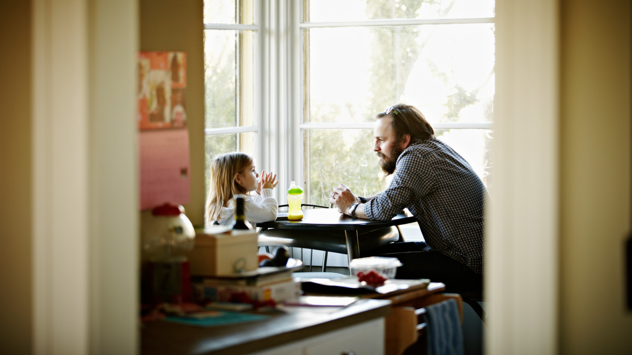 Father and daughter sitting at kitchen table near window in discussion