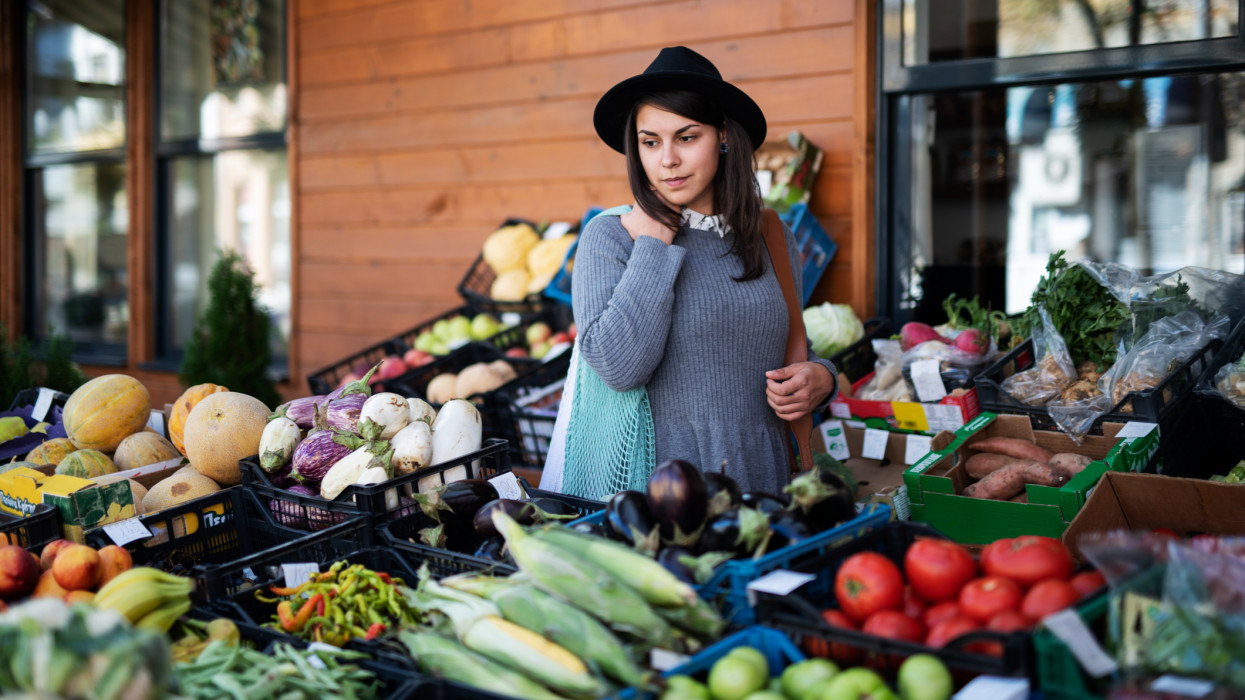 Young woman buying fruit and vegetables at outside market, she looking away.