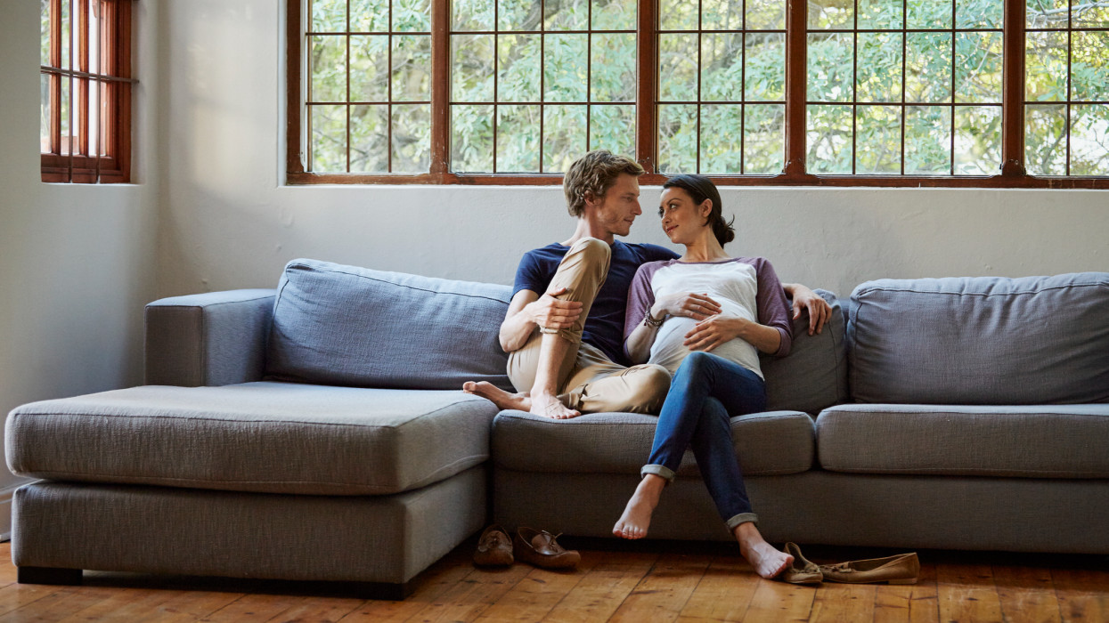 Loving expectant couple looking at each other while sitting on sofa at home