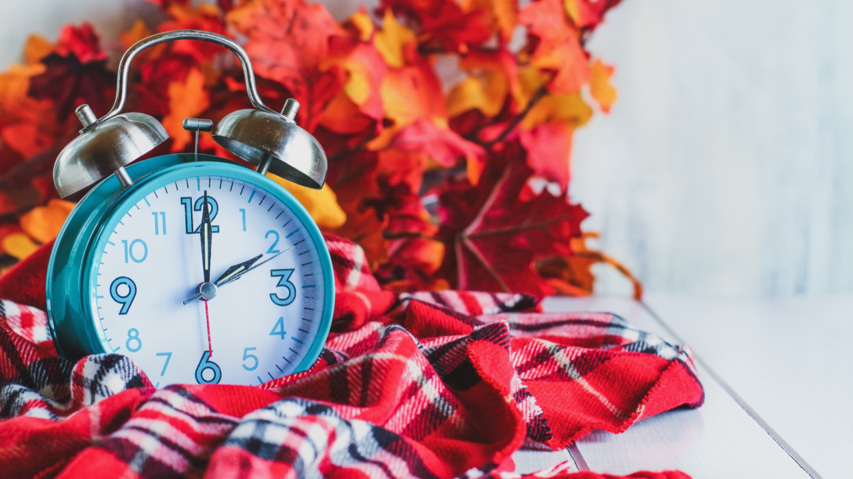 Daylight savings time concept. Set your clocks back with this retro beautiful alarm clocks set to 2 am over rustic white background with red plaid scarf and autumn leaves. Free space for text.