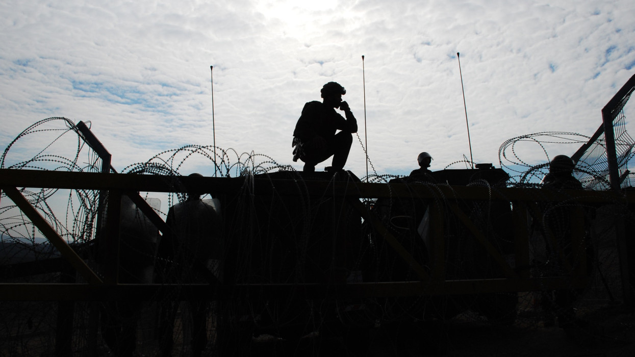Israeli soldiers guarding a barrier, silhouetted against afternoon sun