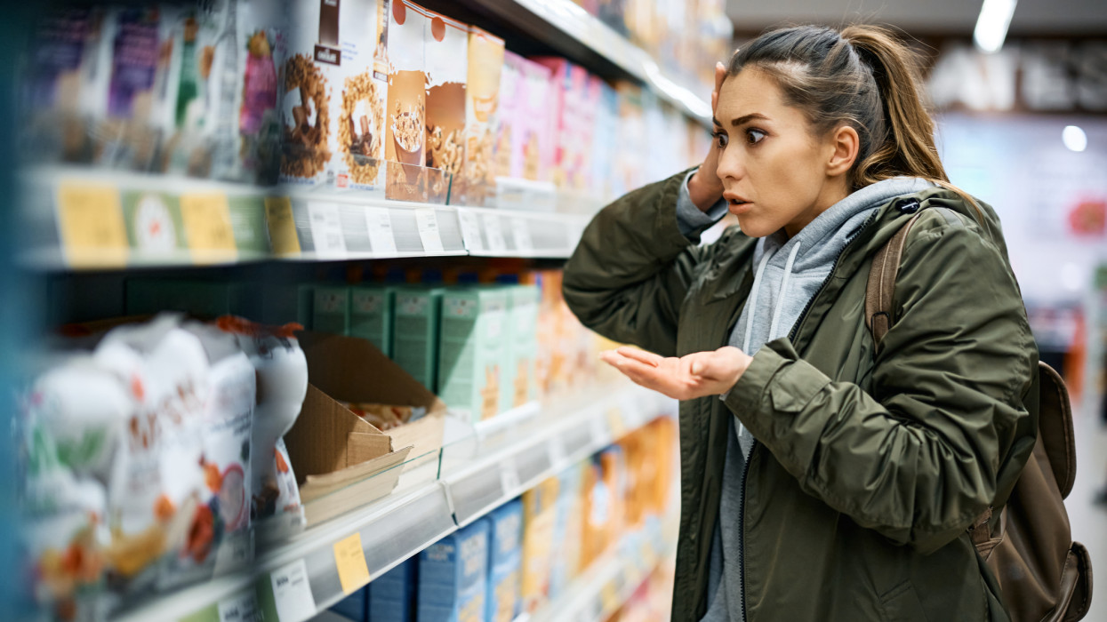 Shocked woman looking at grocery prices in disbelief while buying in supermarket.