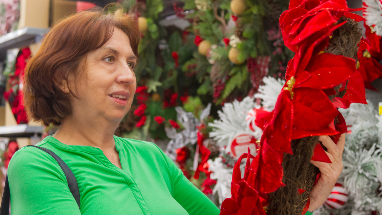 Christmas Latin Experience in United States of America USA.Close portrait of happiness latin mature woman shopping an artificial Christmas wreath in a megastore in United States, wearing a green sweater standing in front of the Christmas decorations in the department store some days before Christmas holidays.
