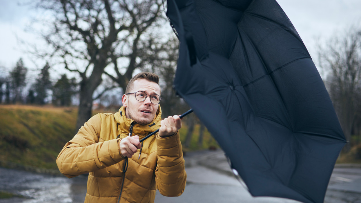 Man holding broken umbrella in strong wind during gloomy rainy day. Themes weather and meteorogy. n