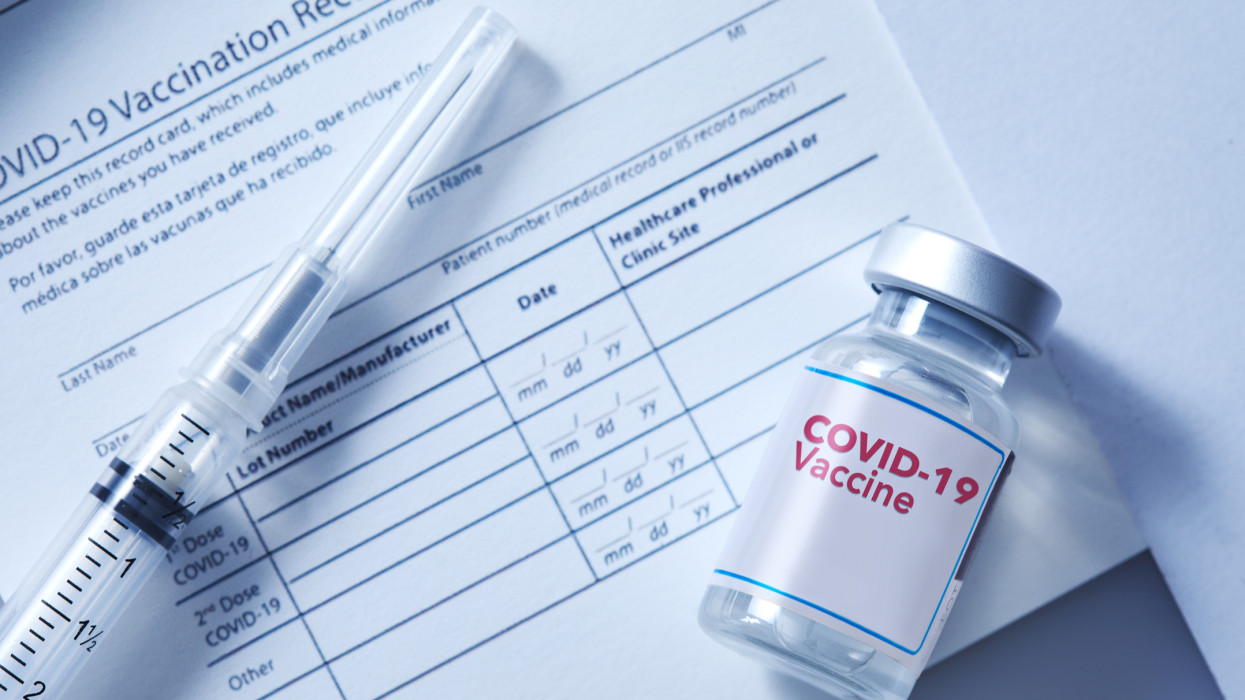 A vial of coronavirus vaccine on a vaccination record card with a syringe on the side