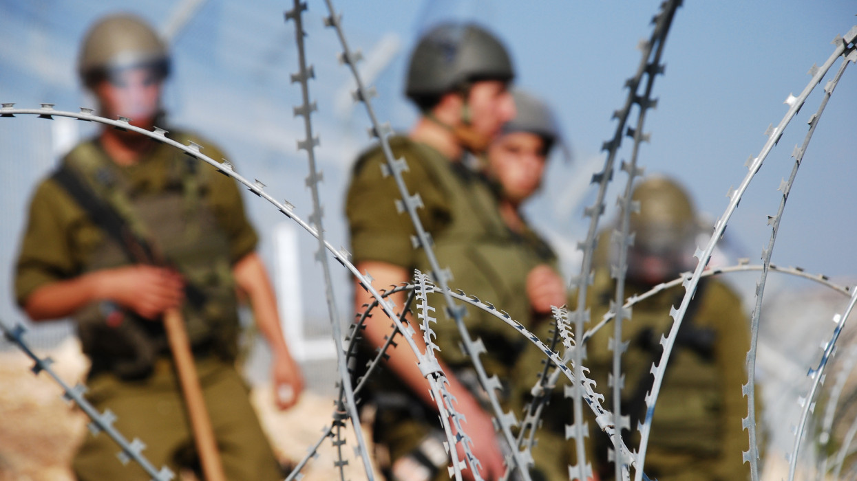 Four Israeli soldiers stand behind razor wire near the Palestinian village of Bilin in the West Bank