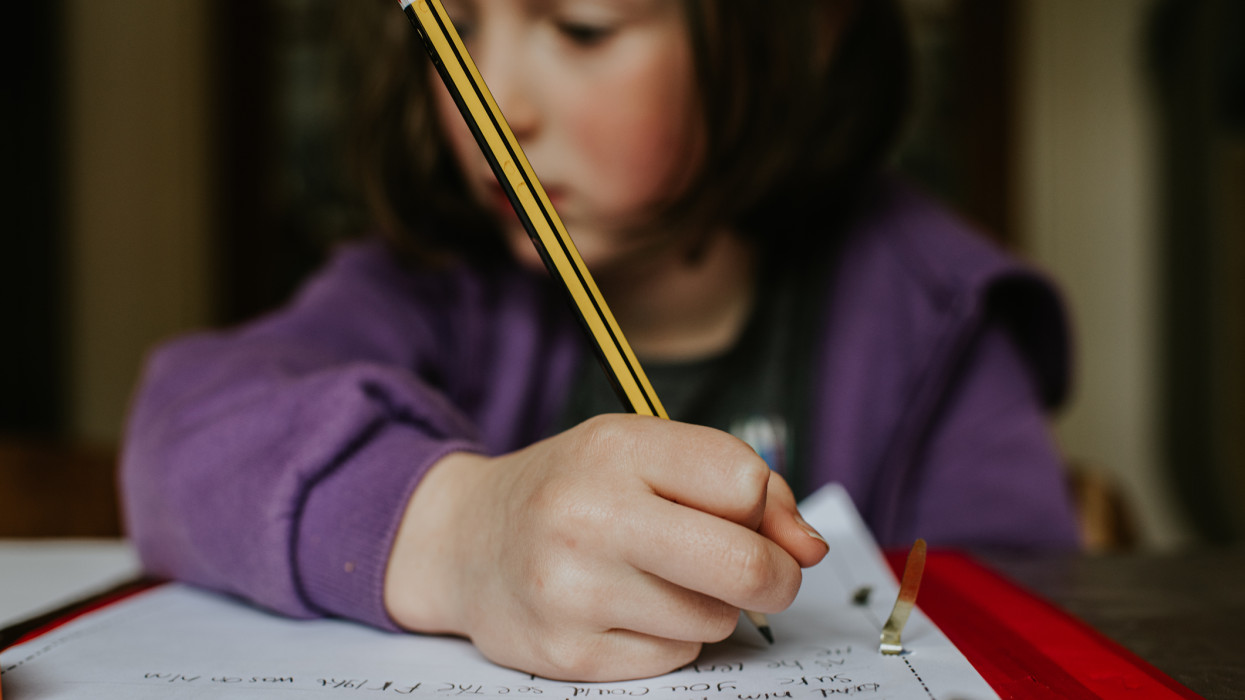 A little girl holds a pencil while she does her homework. Focus on the pencil.