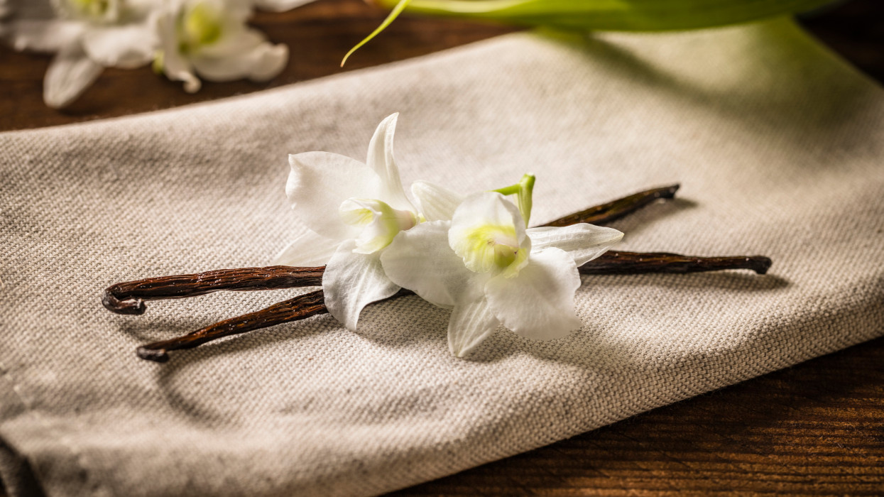 Front view of two vanilla beans and flower on a wooden table