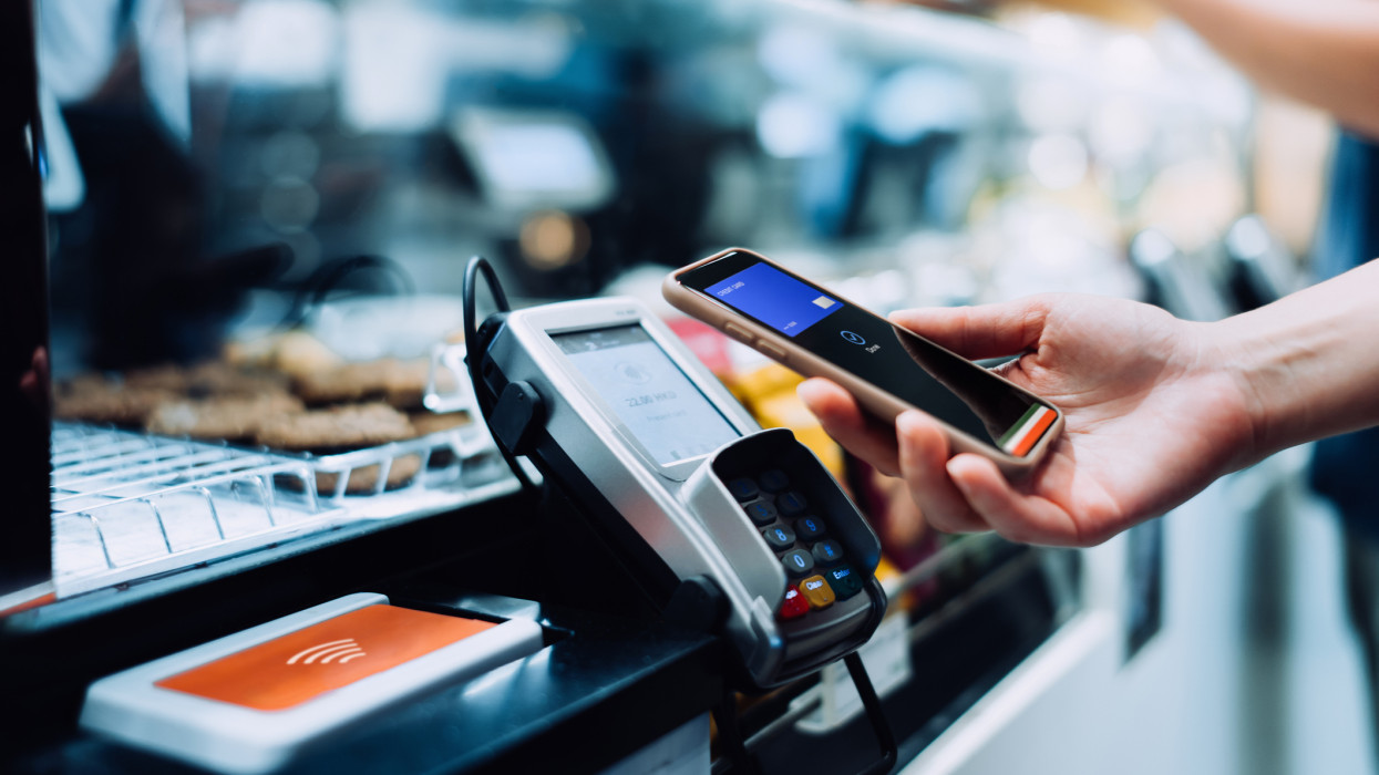 Close up of a womans hand paying with her smartphone in a cafe, scan and pay a bill on a card machine making a quick and easy contactless payment. NFC technology, tap and go concept
