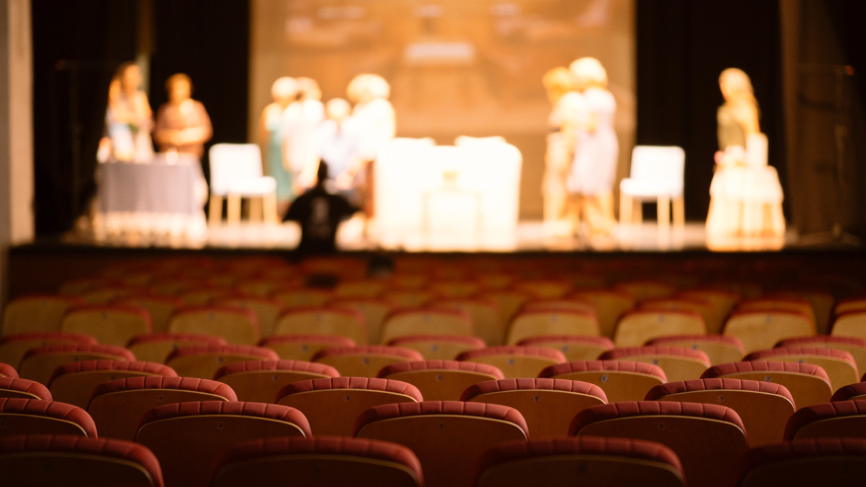 Empty theater red seats and a theater company  in a rehearsal session defocused at background