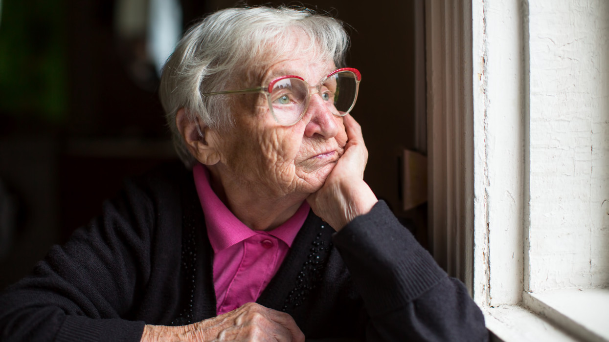 Elderly woman in glasses thoughtfully looking out the window.