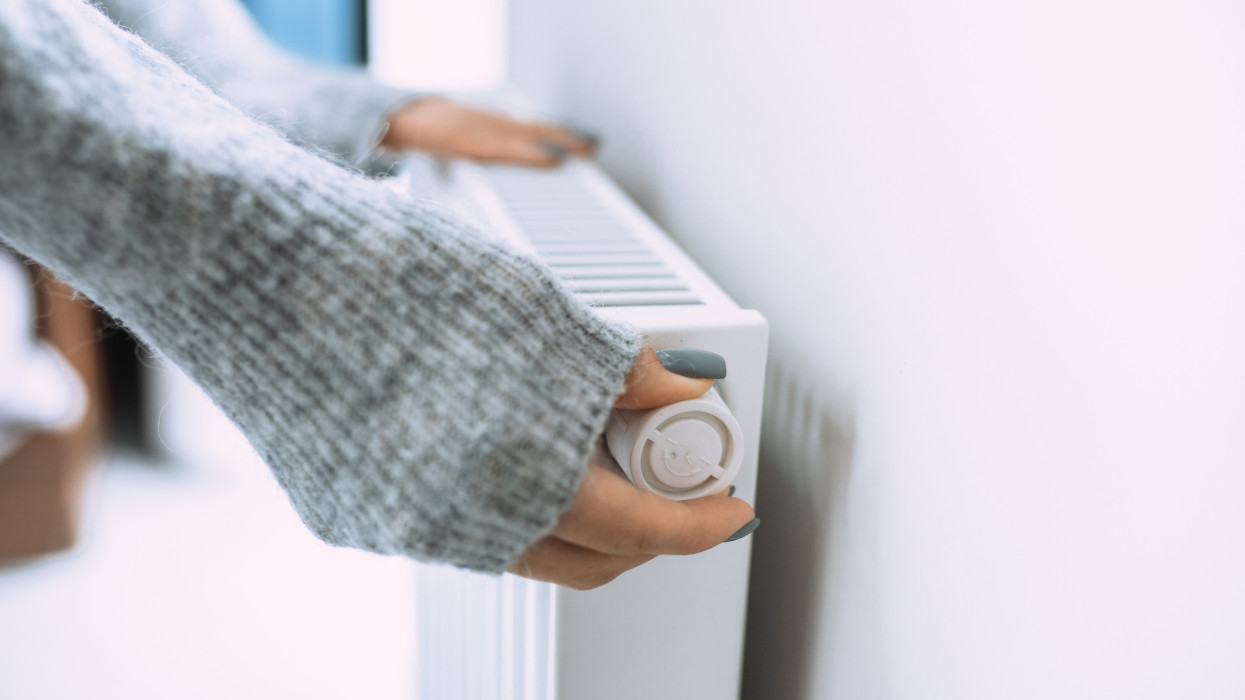 Unrecognizable woman hands in gray sweater touching and setting radiator thermostat regulator