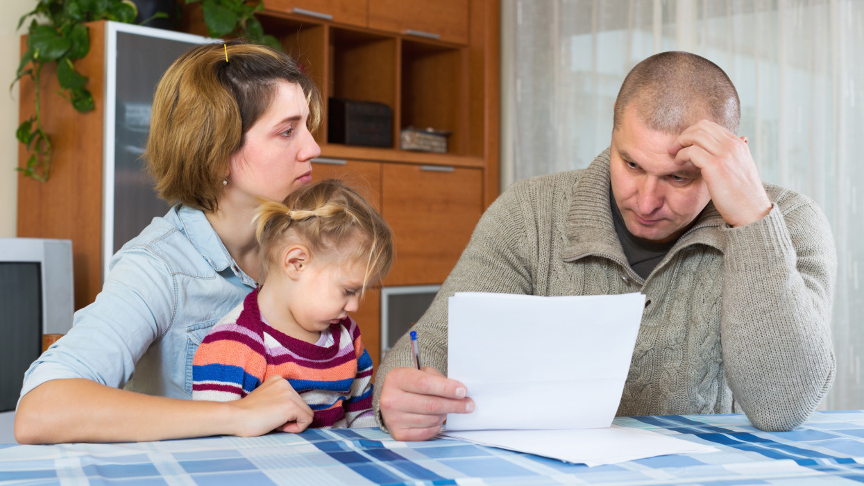 Serious couple with little girl counting budget at home