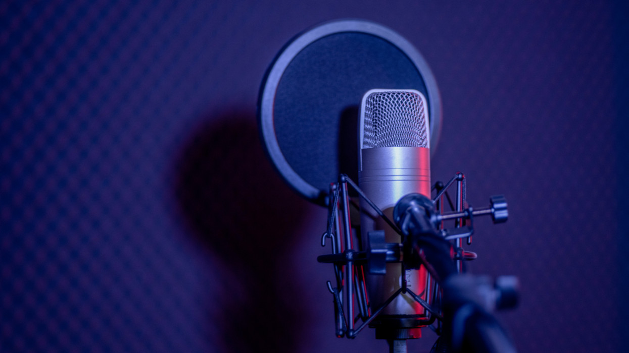 Microphone Condenser, gold mic with filter hang over sound absorbing wall room in dark audio studio, low exposure shadow silhouette studio lighting