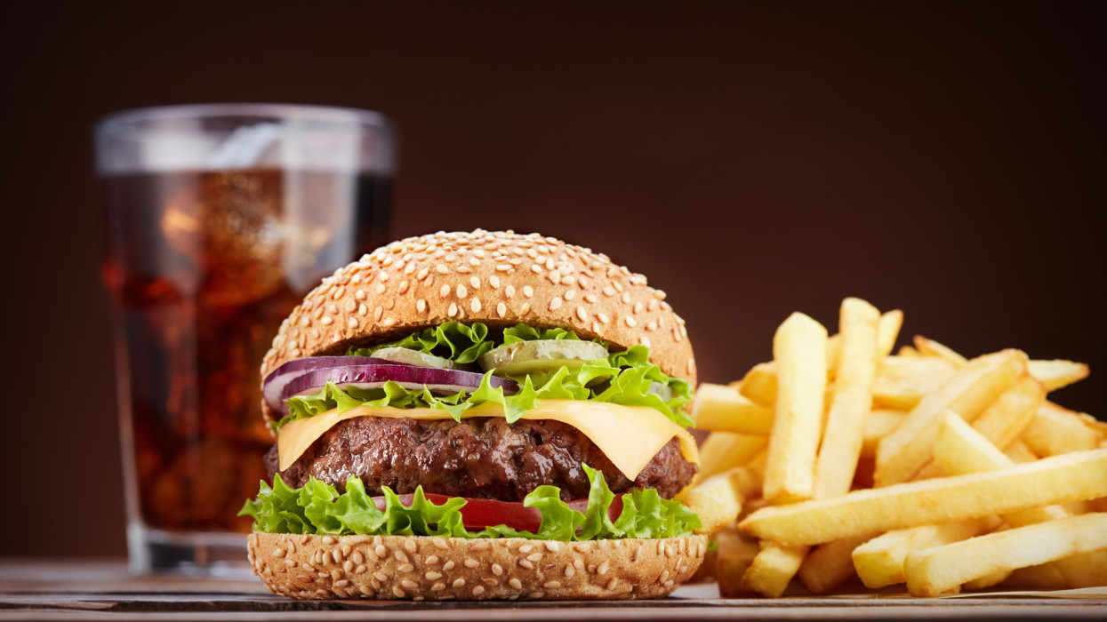 fresh cheeseburger with glass of cola and pile of french fries on wooden table