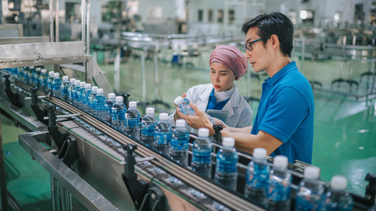 Asian Malay inspector examining quality of mineral water in mineral water factory production line