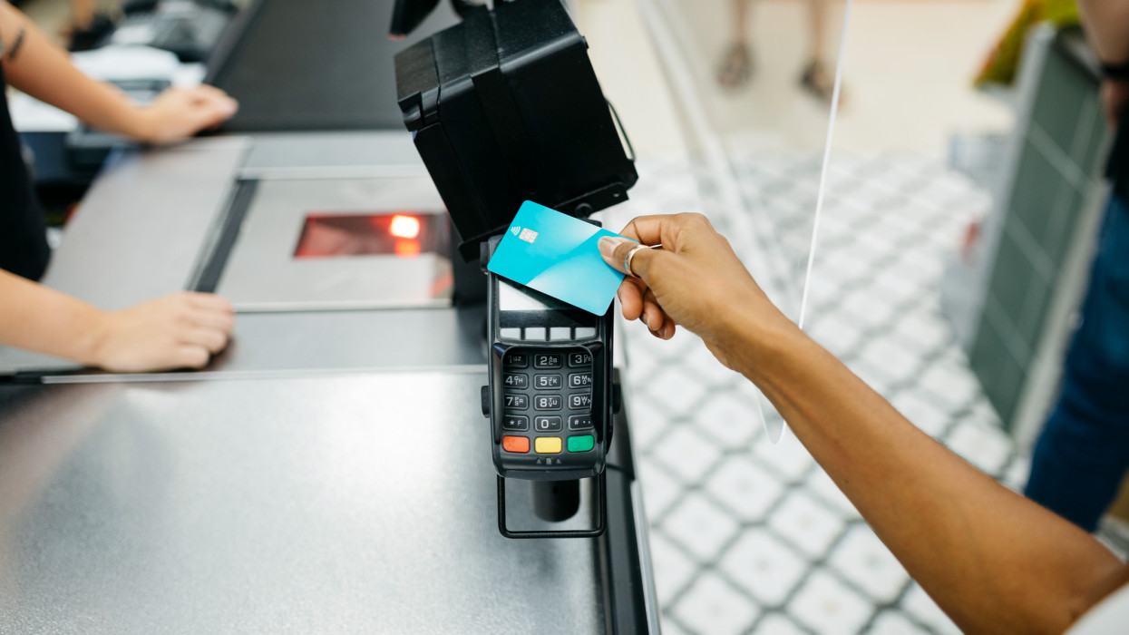 Közelkép egy fekete női emberi kézről, amint hitelkártyával fizet egy pénztárgépen egy szupermarketben