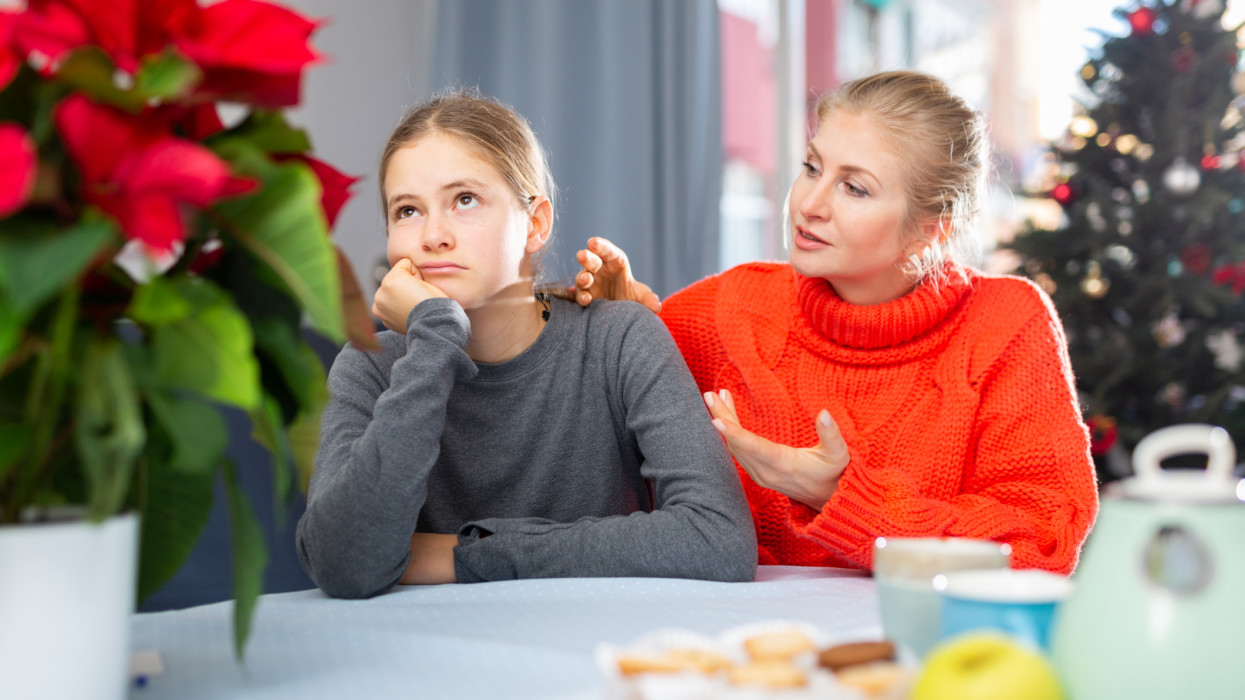 Mother and unhappy teenage girl sitting after quarrel at home after New Year, mother consoles daughter