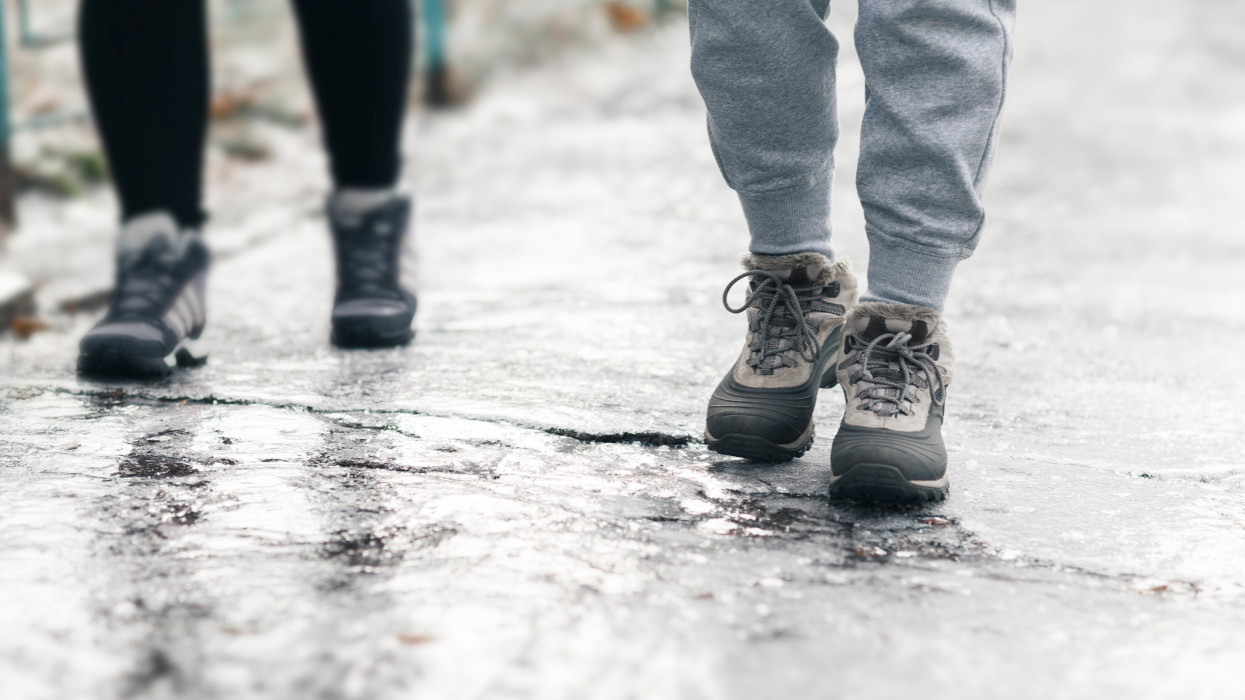Pedestrians glide along the icy sidewalk. Winter ice on footpaths.
