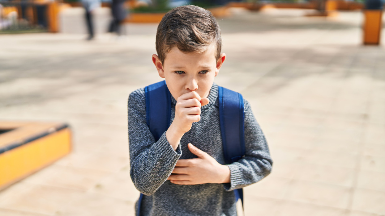 Blond child student coughing at park