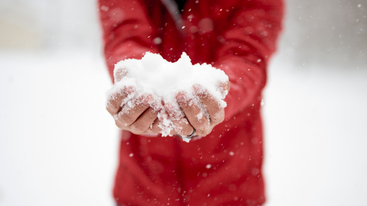 A closeup shot of a male holding snow with his two hands and a blurred background