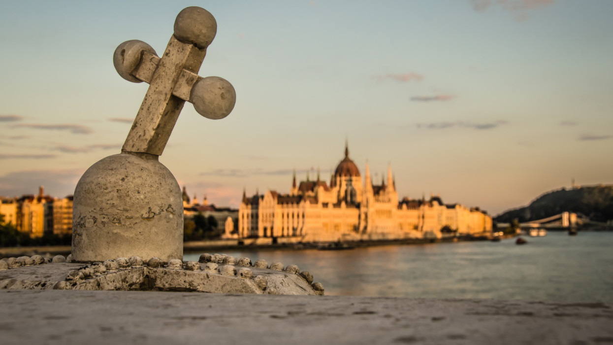 Closeup of a stone Hungarian Cross with the Hungarian Parliament building in the background.