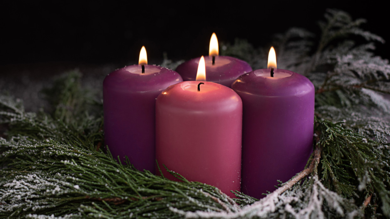 Snowy wreath with four burning purple advent candles on a dark wooden background, Christmas catholic tradition.