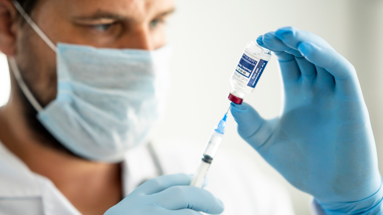 Close up of a medical professional holding a syringe drawing vaccine from a vial to prepare for injection