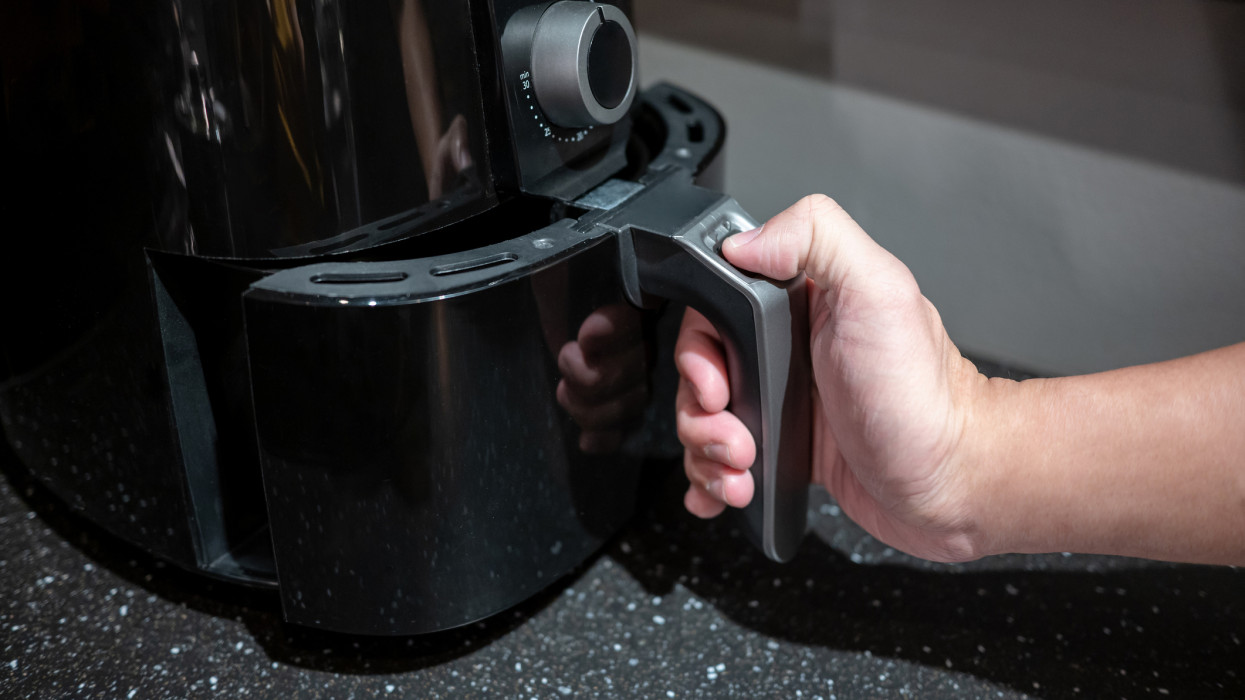 Male hand holding an electric air fryer handle in the kitchen. Home appliance for healthy cooking lifestyle.
