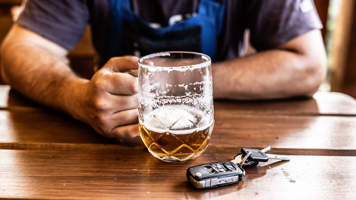 An irresponsible driver is sitting in a pub, drinking beer before driving a car.
