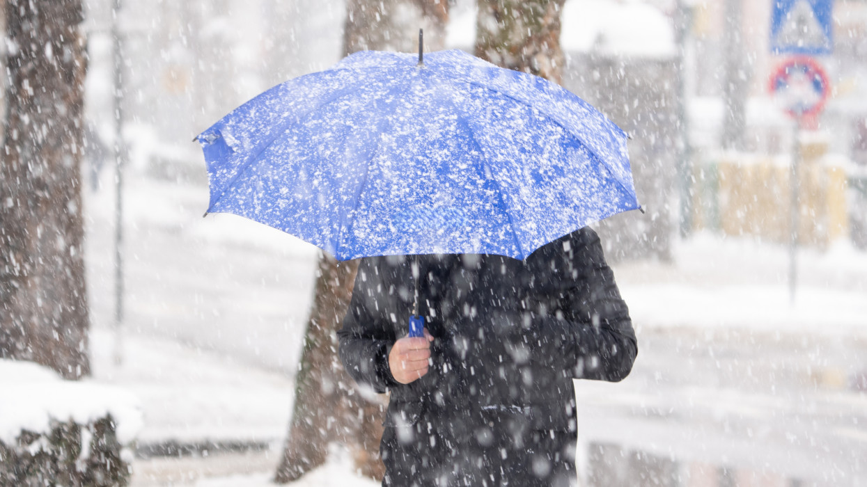 Man with umbrella under snow on city street