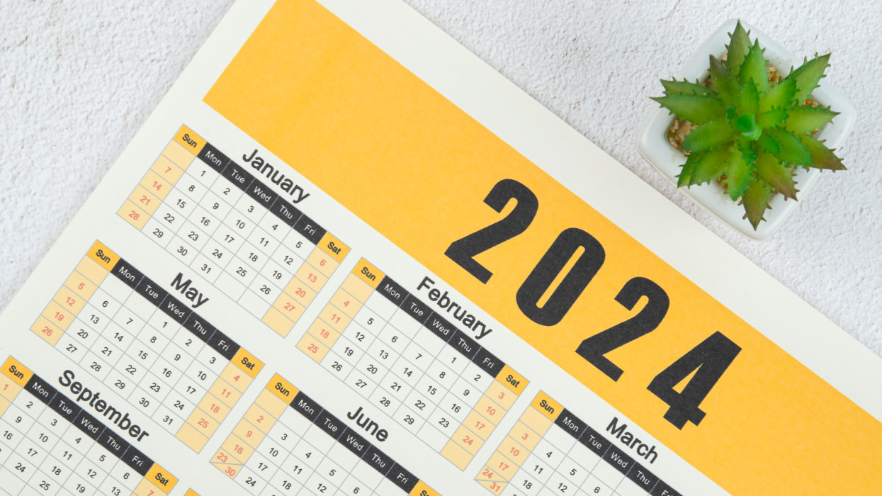 Top views of the calendar desk 2024 is the month for the organizer to plan and deadline with houseplant against a wooden table background.