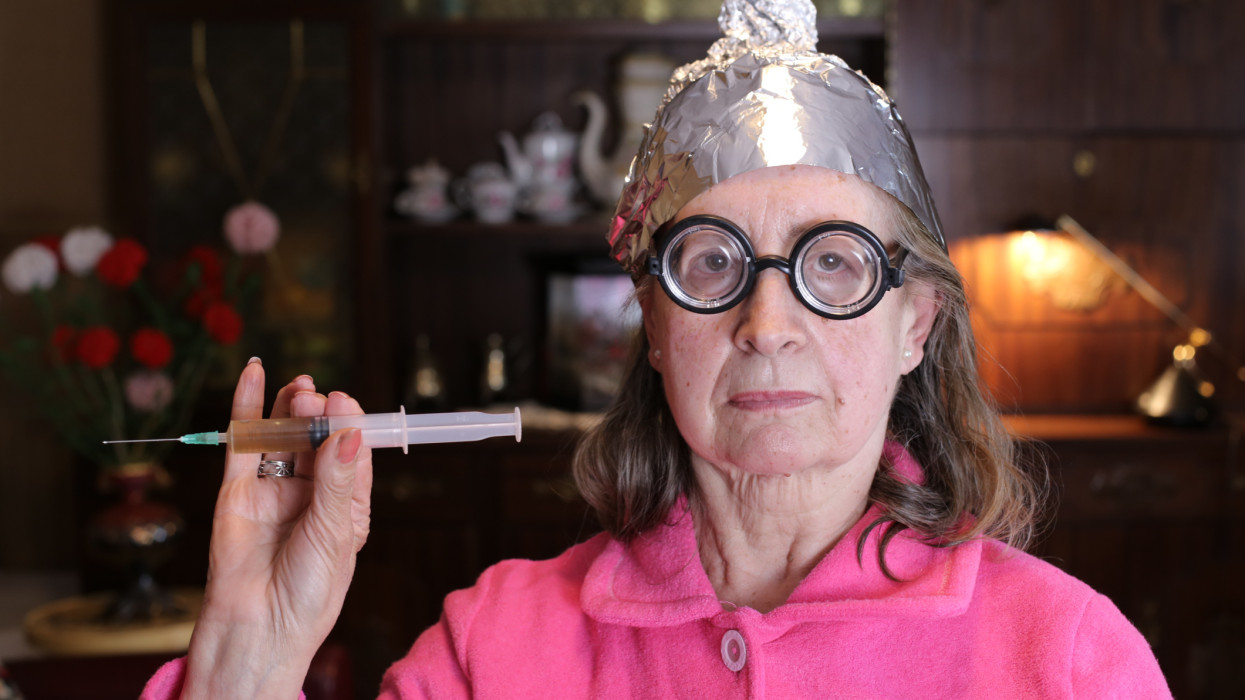 Senior woman wearing tin foil hat holding syringe.