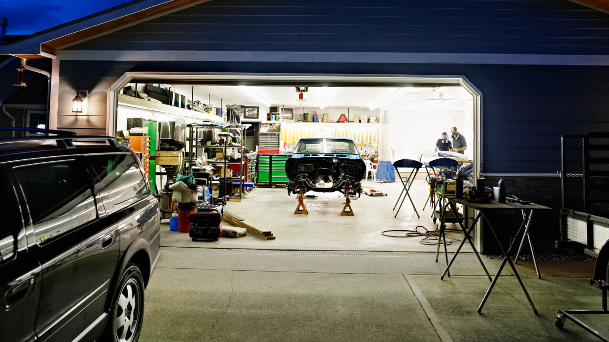 View of garage at night with two friends working on restoring classic car