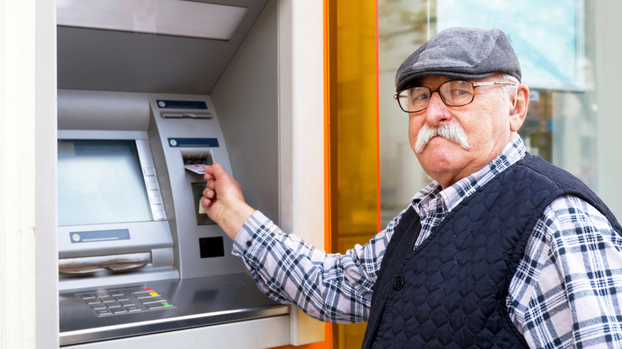 elderly man inserting credit card to ATM outdoor