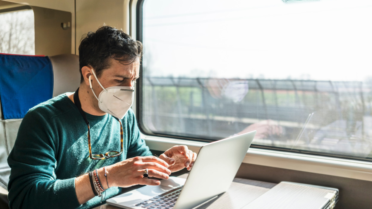 Businnesman with covid-19 protective mask working with laptop while traveling by train