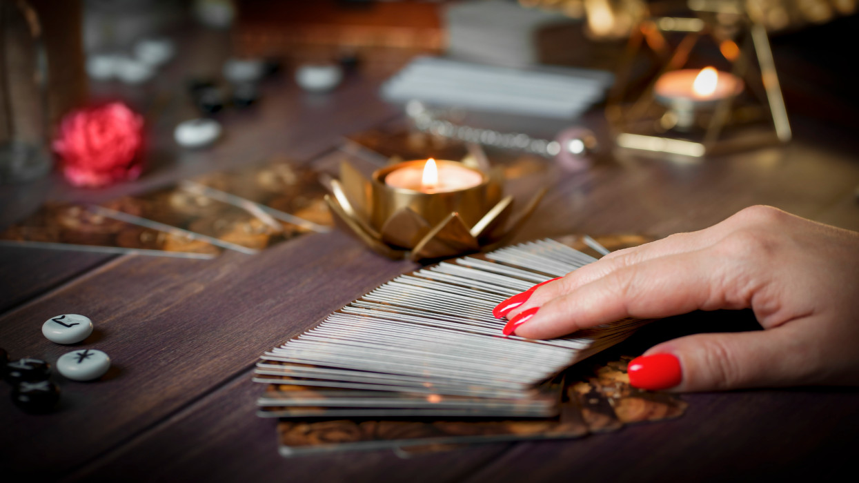 Tarot card reader arranges cards in a card spread.Fortune-telling on traditional tarot cards on the table with a candle. Selective focus.