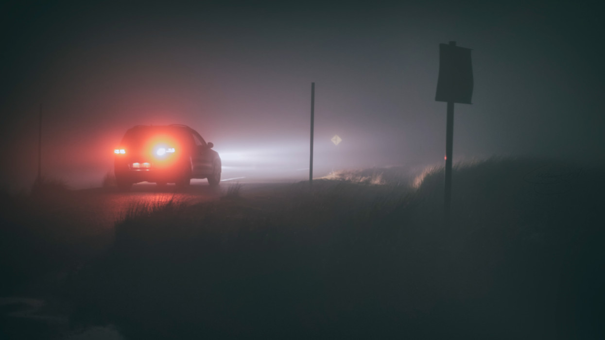A car drives on through thick fog on a country road at night