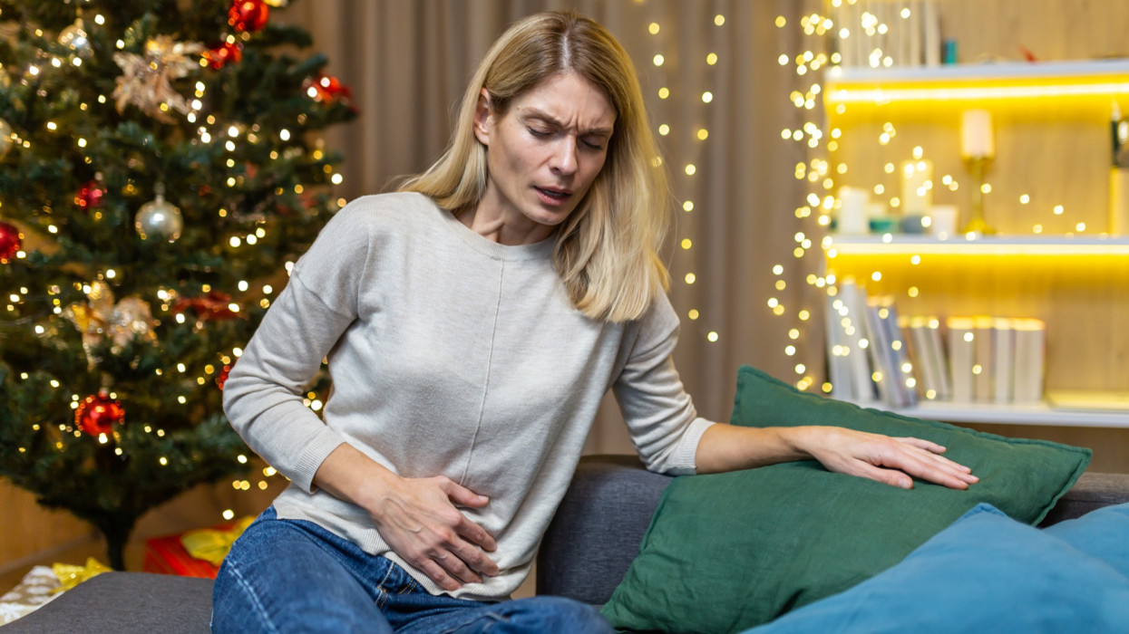 Woman abdominal pain and nausea on New Years Eve sitting at home on the sofa against the background of a Christmas tree. Poisoning, heartburn, menstrual pain syndrome feels bad.