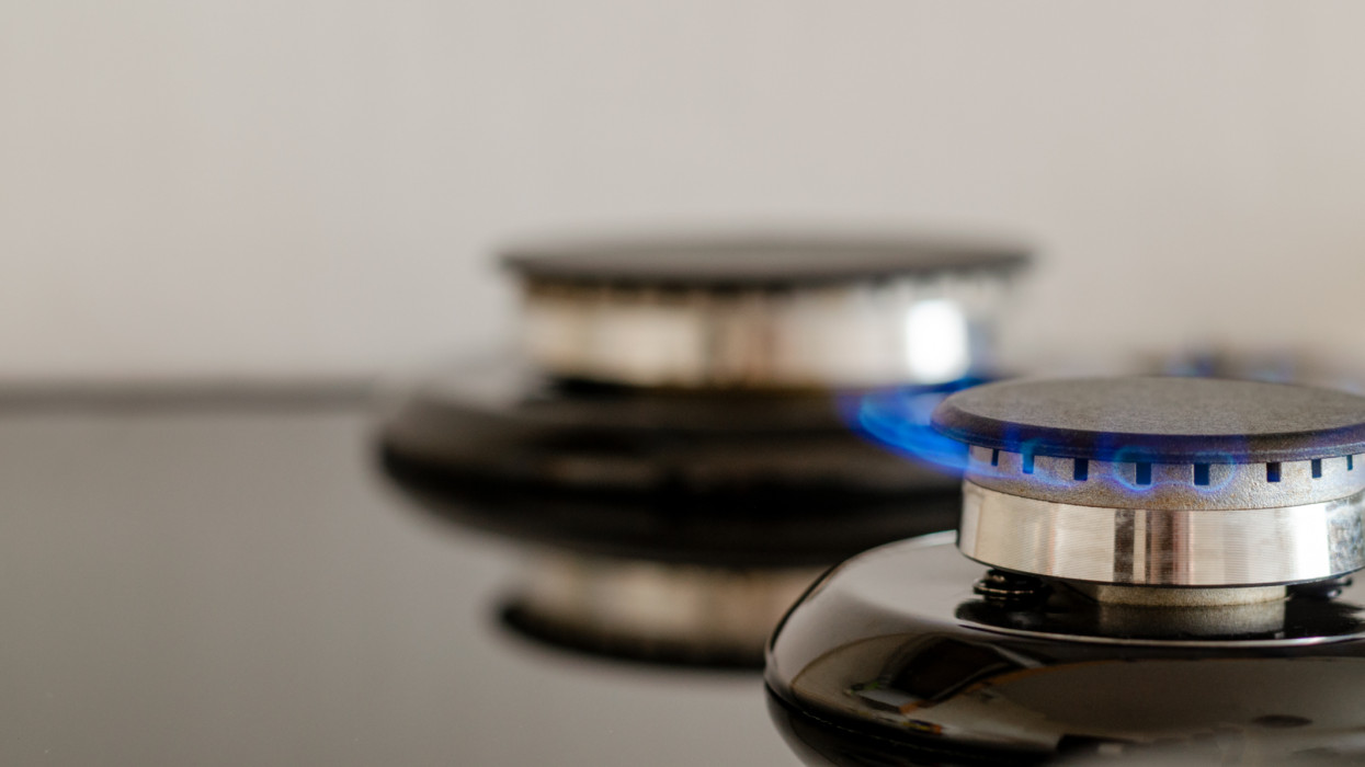 Two gas burners with a flame on one of them. Kitchen stove on a blurred light background. Cropped close-up image