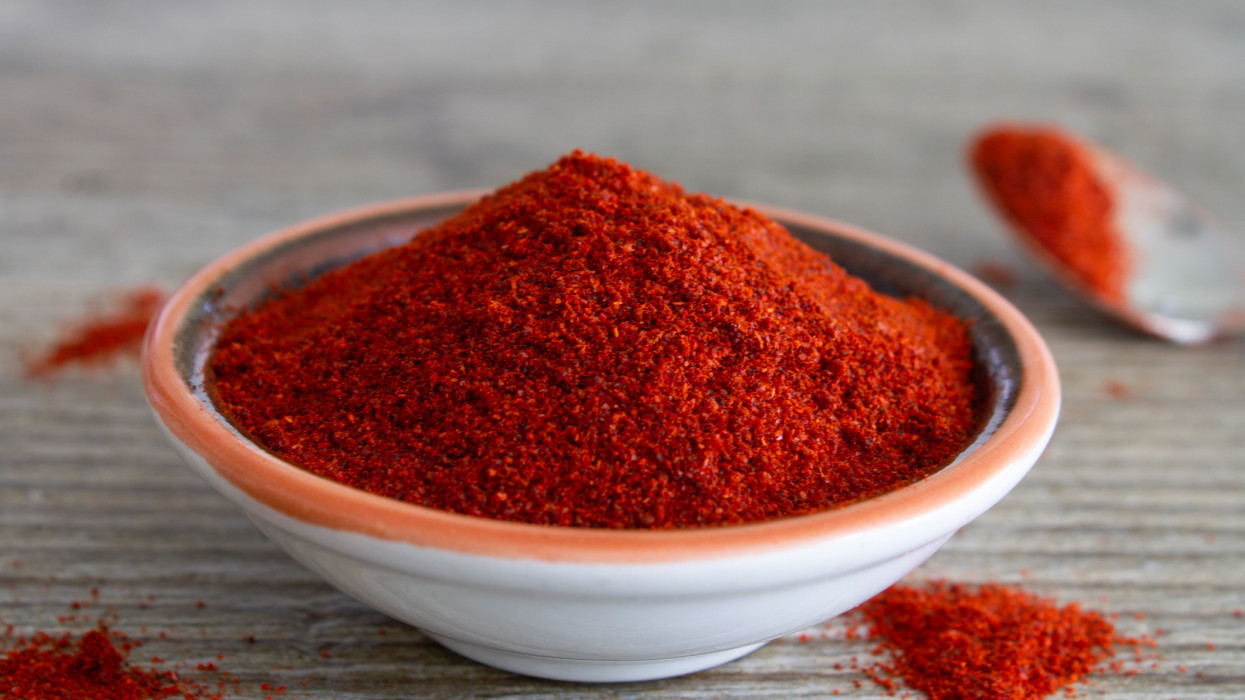 Paprika spice in a small dish on a rustic wooden grey table. Close up view with copy space. Stock photo.