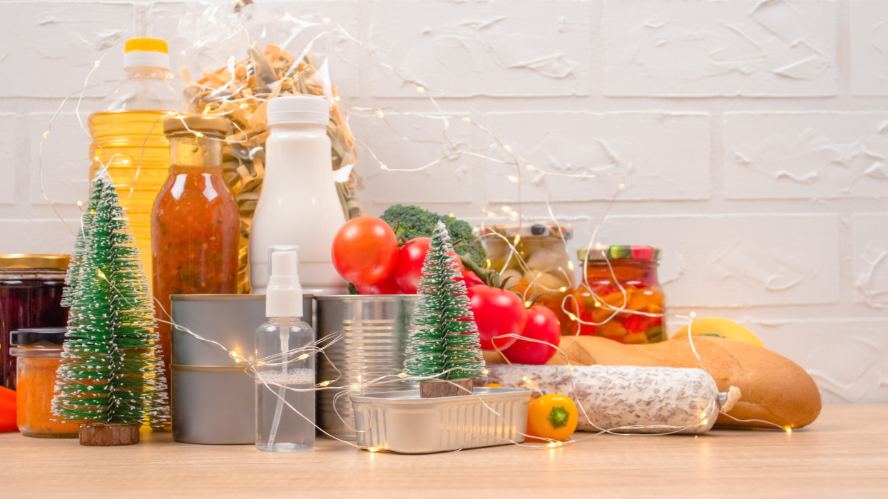 Christmas donations - food donations on light background with copyspace - pasta, fresh vegatables, canned food, baguette, cooking oil with Christmas decorations. Food bank, selective focus